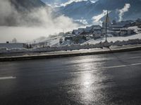 a red fire hydrant is sitting in the middle of a snow covered street with mountains behind it