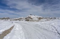 a road in the middle of snowy mountains near a mountaintop with a lighthouse on the top