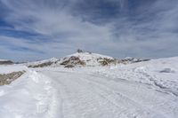 a road in the middle of snowy mountains near a mountaintop with a lighthouse on the top