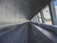 a car traveling down a snow covered mountain road between two large buildings under an overpass