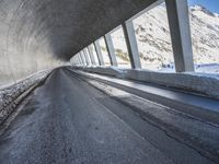 a car traveling down a snow covered mountain road between two large buildings under an overpass