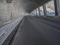 a car traveling down a snow covered mountain road between two large buildings under an overpass