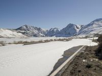 a very long road with some snow on the sides and mountains behind it as seen in this photograph