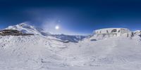 a snowy mountain with ski slopes and buildings in the background under a blue sky with a moon