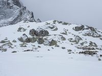 a person with backpacks on walking up a mountain covered in snow and rocks, in the distance, with mountains with snowcappeds