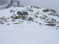 a person with backpacks on walking up a mountain covered in snow and rocks, in the distance, with mountains with snowcappeds