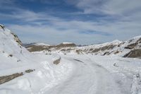 a dirt road near the snowy mountains covered in snow near the bottom of the hill