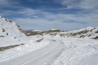 a dirt road near the snowy mountains covered in snow near the bottom of the hill