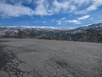 a view of the snowy mountains from a parking lot with broken tarmacs and the road is empty