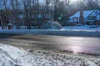 there is snow all over the ground by a road and some houses in the background