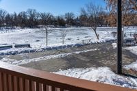 snow is on the ground from the balcony in front of the house with benches and trees in the background