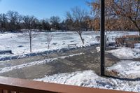 snow is on the ground from the balcony in front of the house with benches and trees in the background