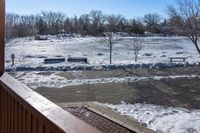 snow is on the ground from the balcony in front of the house with benches and trees in the background