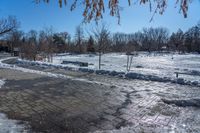 a park area covered with snow and ice covered ground and benches next to a fence