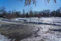 a park area covered with snow and ice covered ground and benches next to a fence