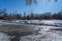 a park area covered with snow and ice covered ground and benches next to a fence