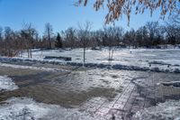 a park area covered with snow and ice covered ground and benches next to a fence