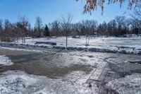 a park area covered with snow and ice covered ground and benches next to a fence