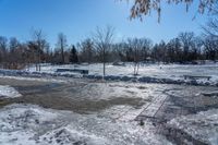 a park area covered with snow and ice covered ground and benches next to a fence