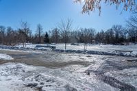 a park area covered with snow and ice covered ground and benches next to a fence