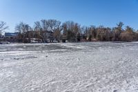 a man is walking across ice covered ground near trees and houses along the lake while looking at something to be seen