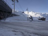 a snowy parking lot covered in snow under a ski lift lift in the background of mountains