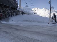 a snowy parking lot covered in snow under a ski lift lift in the background of mountains