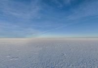 a snowy plain is shown with white footprints in the snow beneath a blue sky and clouds