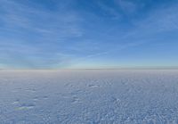 a snowy plain is shown with white footprints in the snow beneath a blue sky and clouds