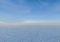 a snowy plain is shown with white footprints in the snow beneath a blue sky and clouds