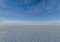 a snowy plain is shown with white footprints in the snow beneath a blue sky and clouds