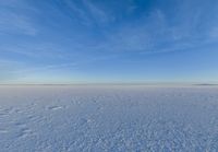 a snowy plain is shown with white footprints in the snow beneath a blue sky and clouds