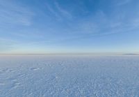 a snowy plain is shown with white footprints in the snow beneath a blue sky and clouds