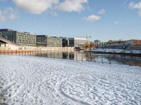 a blue sky and some buildings in a park by the water with snow on the ground