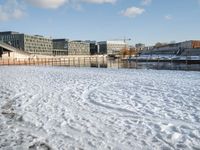 a blue sky and some buildings in a park by the water with snow on the ground