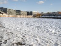 a blue sky and some buildings in a park by the water with snow on the ground