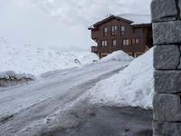 the snow covers the road and walkway to a house on top of the mountain side