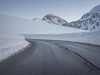 a paved road with some rocks on the side and snow on top of it with mountains in the background