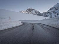 a paved road with some rocks on the side and snow on top of it with mountains in the background