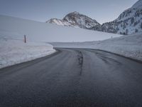 a paved road with some rocks on the side and snow on top of it with mountains in the background