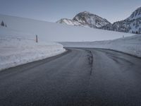a paved road with some rocks on the side and snow on top of it with mountains in the background