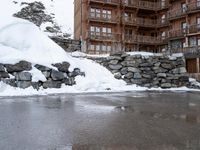 snow covering rocks are piled in front of a brown building next to the water in the street