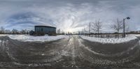 a view of a snowy road with a barn in the distance and some buildings near by