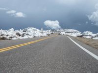 snow covers the roadway and snowy mountains on a sunny day, with a yellow warning sign in front of it