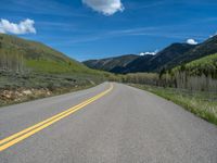 the road is paved with yellow markings and has a snowy mountain range in the background