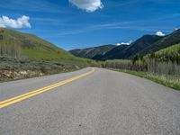 the road is paved with yellow markings and has a snowy mountain range in the background