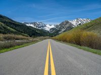 the road is paved with yellow markings and has a snowy mountain range in the background