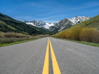 the road is paved with yellow markings and has a snowy mountain range in the background