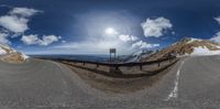 the 360 - view lens picture shows the road and mountains in the distance with clouds