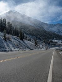 a single motorcycle is driving in the middle of a road between mountains in the snow